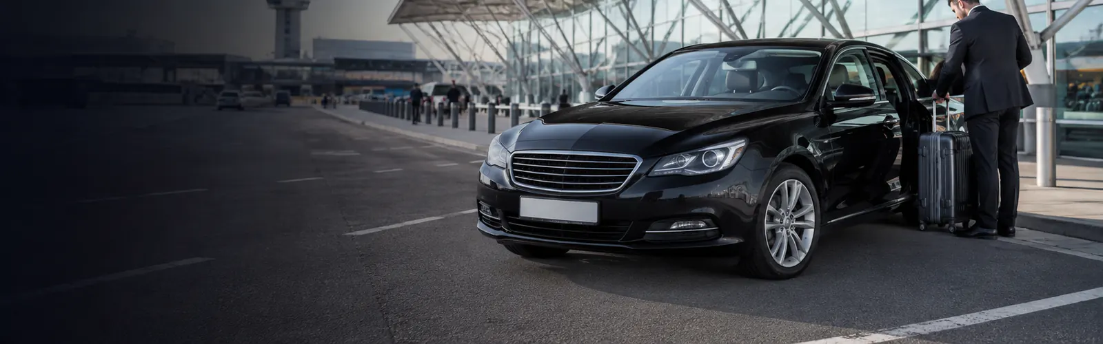 Black airport transfer car with driver and luggage outside a modern Heathrow terminal